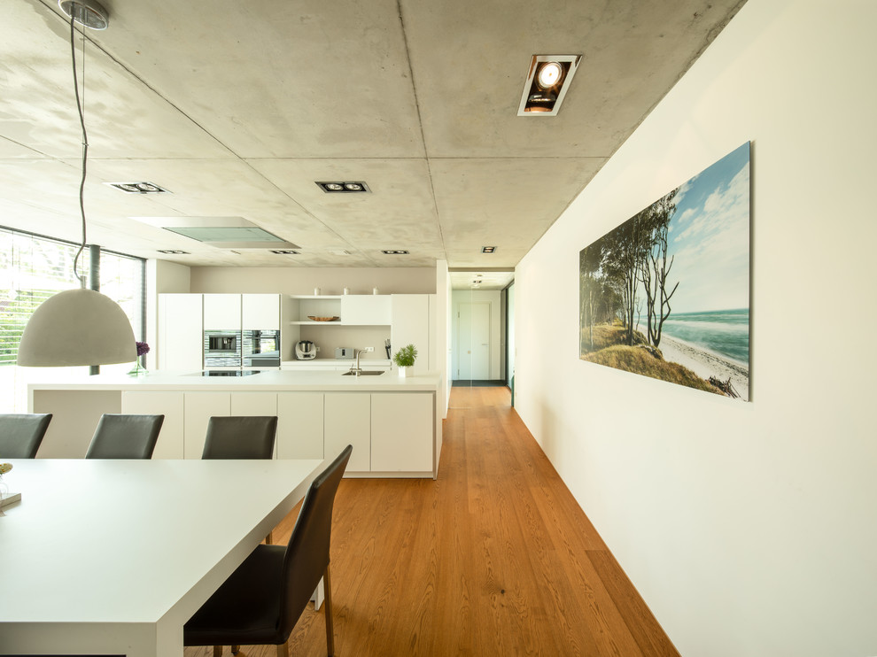 Photo of a large modern galley open plan kitchen in Stuttgart with flat-panel cabinets, white cabinets, laminate benchtops, white splashback, with island, white benchtop, stainless steel appliances, medium hardwood floors, brown floor and a drop-in sink.