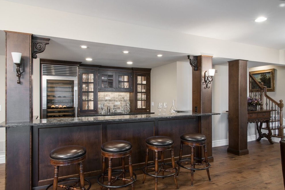 Mid-sized traditional galley seated home bar in St Louis with raised-panel cabinets, dark wood cabinets, granite benchtops, multi-coloured splashback, stone tile splashback and medium hardwood floors.