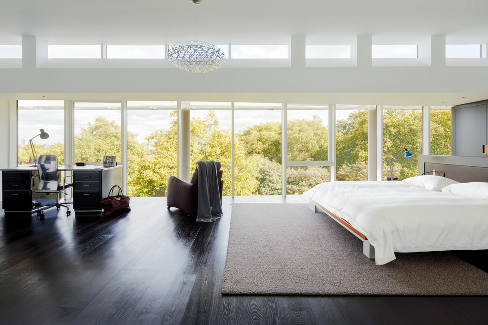Expansive contemporary master bedroom in London with white walls, dark hardwood floors, no fireplace and brown floor.