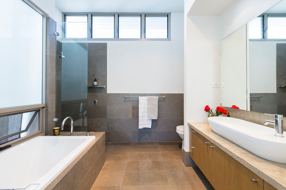 Inspiration for a mid-sized contemporary 3/4 bathroom in Perth with flat-panel cabinets, medium wood cabinets, a drop-in tub, a curbless shower, a one-piece toilet, gray tile, ceramic tile, white walls, a vessel sink, beige floor and a hinged shower door.