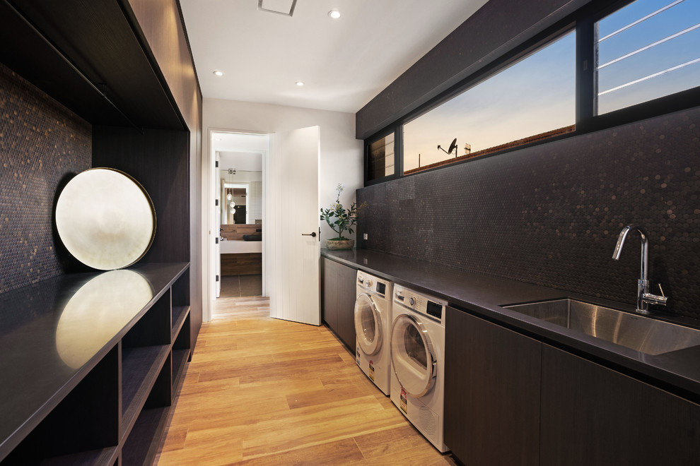 This is an example of a large contemporary galley dedicated laundry room in Central Coast with an undermount sink, flat-panel cabinets, dark wood cabinets, solid surface benchtops and black benchtop.