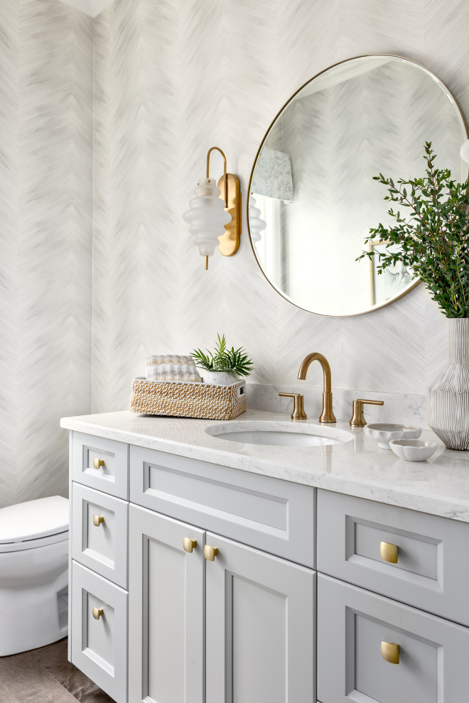 Inspiration for a large traditional powder room in Vancouver with recessed-panel cabinets, grey cabinets, a one-piece toilet, grey walls, dark hardwood floors, a wall-mount sink, engineered quartz benchtops, brown floor, white benchtops, a built-in vanity and wallpaper.