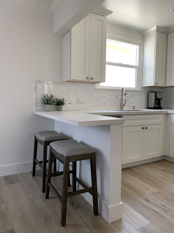 Small transitional u-shaped separate kitchen in Orange County with a double-bowl sink, shaker cabinets, white cabinets, quartz benchtops, grey splashback, porcelain splashback, stainless steel appliances, vinyl floors, a peninsula, beige floor and white benchtop.