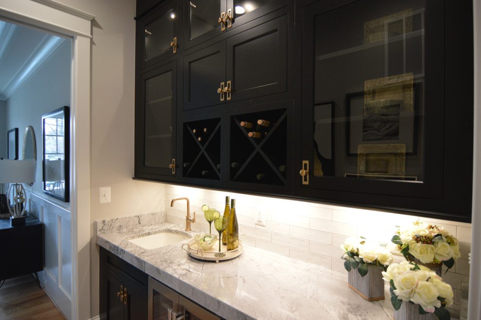 Inspiration for a mid-sized transitional single-wall wet bar in DC Metro with an undermount sink, shaker cabinets, black cabinets, quartz benchtops, white splashback, ceramic splashback, light hardwood floors, brown floor and grey benchtop.