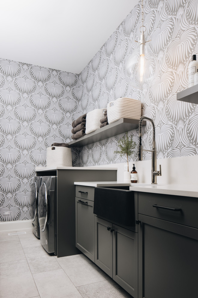 This is an example of a large transitional single-wall dedicated laundry room in Chicago with a drop-in sink, shaker cabinets, black cabinets, multi-coloured walls, a side-by-side washer and dryer, grey floor, beige benchtop and wallpaper.