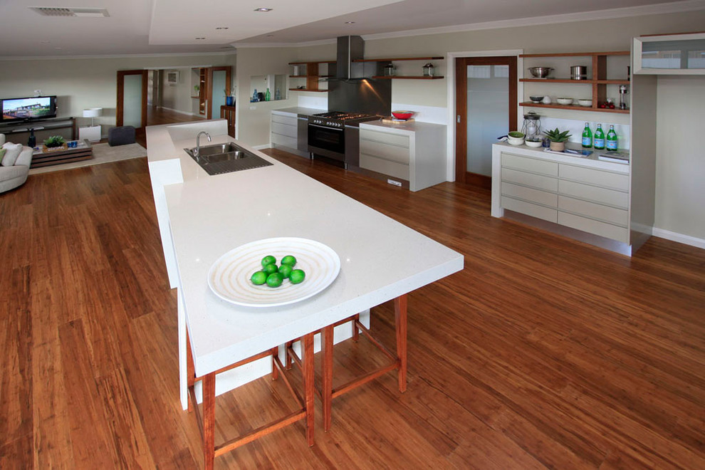Example of a large transitional galley medium tone wood floor and brown floor open concept kitchen design in DC Metro with a drop-in sink, flat-panel cabinets, beige cabinets, quartz countertops, white backsplash, glass sheet backsplash, stainless steel appliances and an island