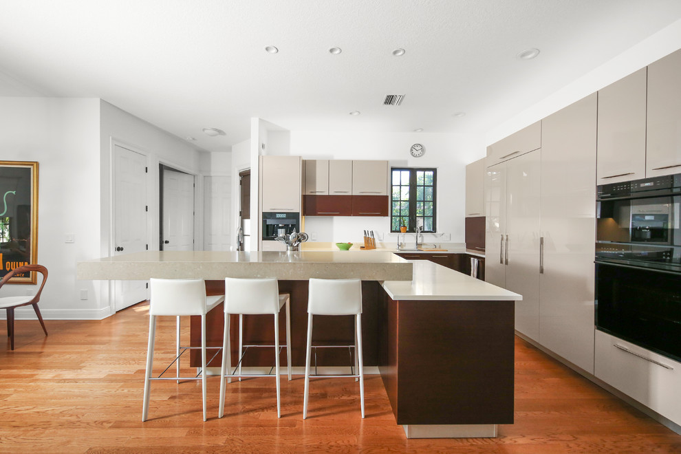 Inspiration for a large contemporary l-shaped open plan kitchen in Other with flat-panel cabinets, beige cabinets, solid surface benchtops, medium hardwood floors, with island, brown floor, white benchtop, an undermount sink and panelled appliances.