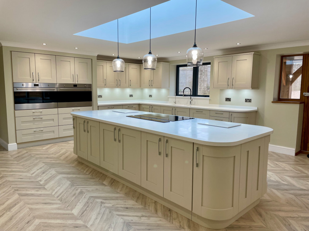Inspiration for a large contemporary u-shaped separate kitchen in Other with an integrated sink, shaker cabinets, grey cabinets, solid surface benchtops, black appliances, light hardwood floors, with island, brown floor and white benchtop.