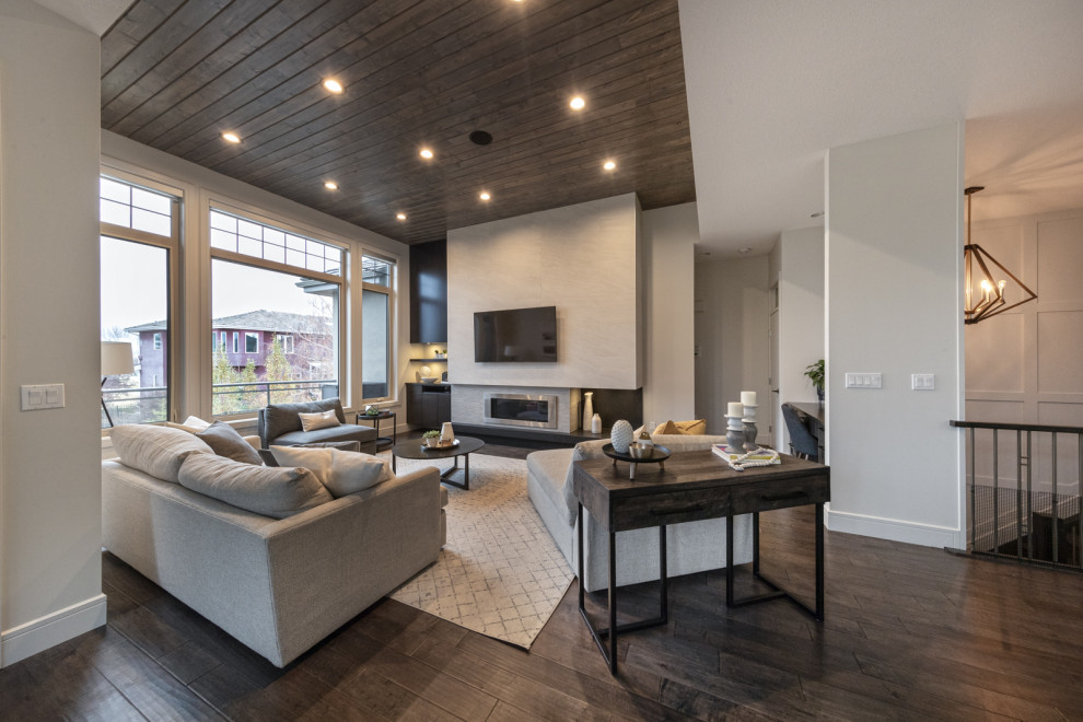 This is an example of a large contemporary open concept living room in Edmonton with grey walls, dark hardwood floors, a standard fireplace, a tile fireplace surround, brown floor, timber, panelled walls and a wall-mounted tv.