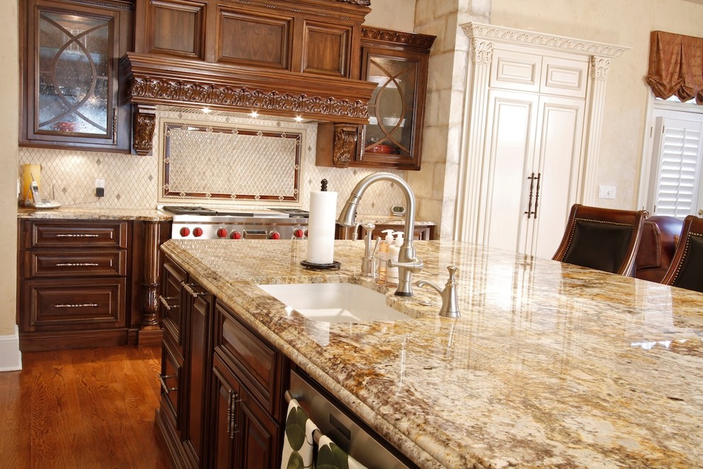 Photo of a large traditional l-shaped open plan kitchen in Atlanta with an undermount sink, raised-panel cabinets, medium wood cabinets, granite benchtops, beige splashback, stone tile splashback, stainless steel appliances, medium hardwood floors, with island and brown floor.