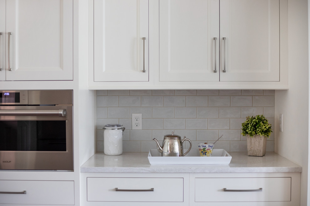 ミルウォーキーにある高級な広いトランジショナルスタイルのおしゃれなキッチン (アンダーカウンターシンク、落し込みパネル扉のキャビネット、白いキャビネット、クオーツストーンカウンター、白いキッチンパネル、モザイクタイルのキッチンパネル、シルバーの調理設備、濃色無垢フローリング、白いキッチンカウンター、表し梁) の写真