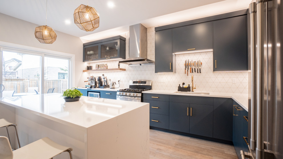 Minimalist l-shaped vinyl floor open concept kitchen photo in Toronto with flat-panel cabinets, blue cabinets, white backsplash, ceramic backsplash, stainless steel appliances, an island, white countertops and quartz countertops