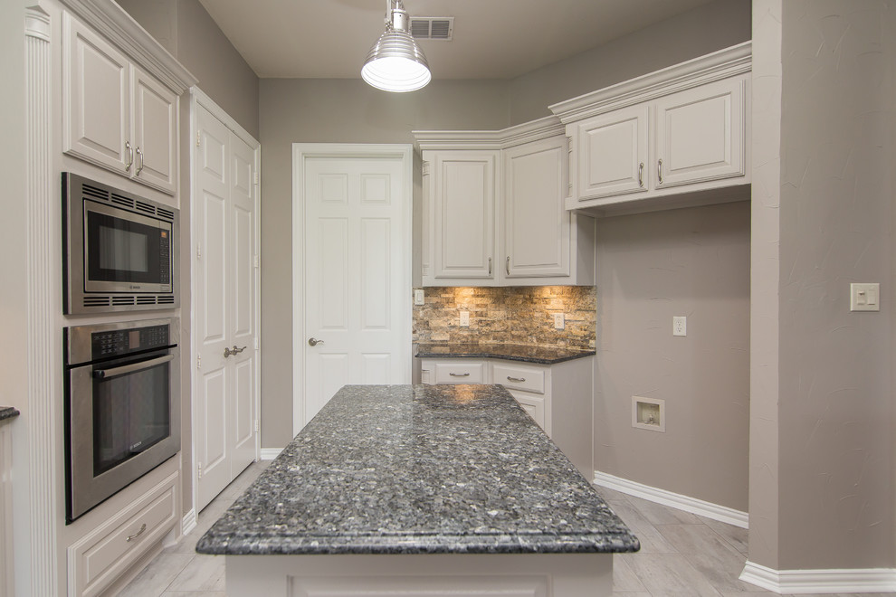 Inspiration for a mid-sized traditional u-shaped eat-in kitchen in Dallas with an undermount sink, raised-panel cabinets, grey cabinets, granite benchtops, beige splashback, stone tile splashback, stainless steel appliances, porcelain floors, with island, grey floor and blue benchtop.