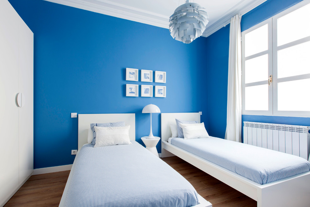 This is an example of a mid-sized transitional guest bedroom in Madrid with blue walls, medium hardwood floors, no fireplace and brown floor.