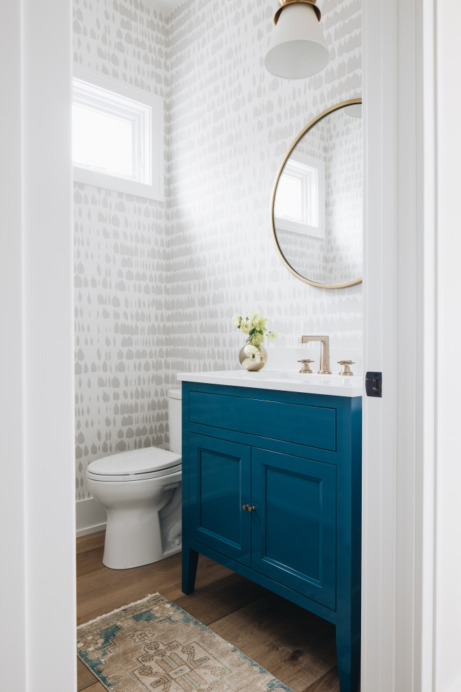 Imagen de aseo de pie costero pequeño con armarios estilo shaker, puertas de armario azules, suelo de madera clara, encimeras blancas y papel pintado