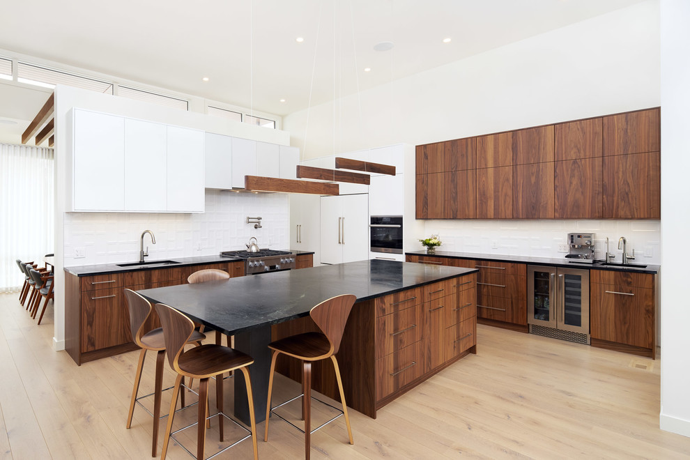 Inspiration for a contemporary l-shaped light wood floor and beige floor open concept kitchen remodel in Calgary with an undermount sink, flat-panel cabinets, dark wood cabinets, soapstone countertops, white backsplash, porcelain backsplash, stainless steel appliances, an island and black countertops