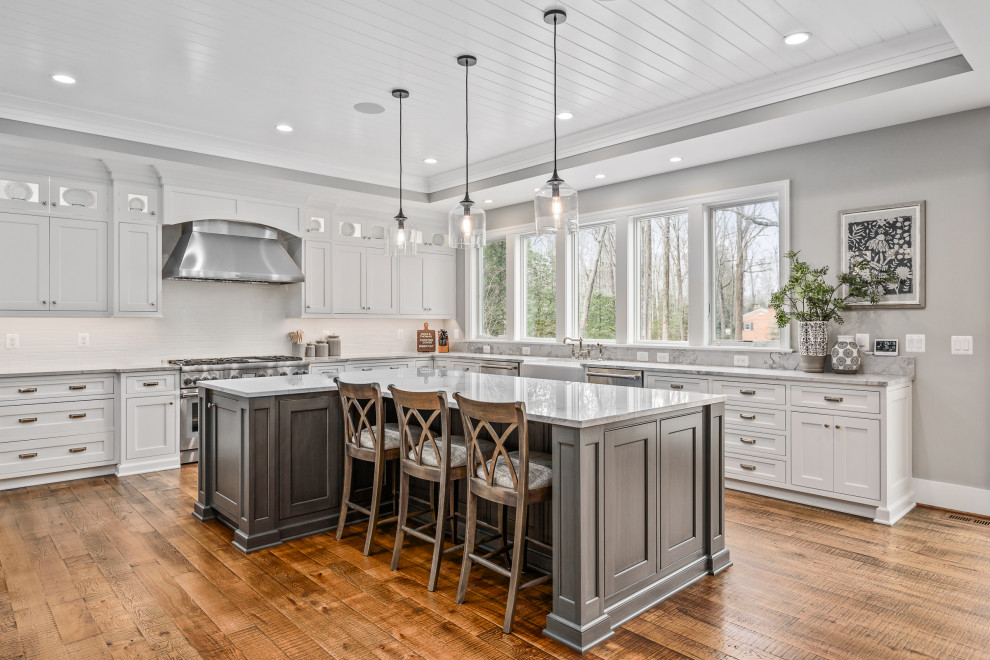 Photo of a traditional l-shaped kitchen in DC Metro with a farmhouse sink, beaded inset cabinets, white cabinets, stainless steel appliances, medium hardwood floors, with island, brown floor, grey benchtop and timber.