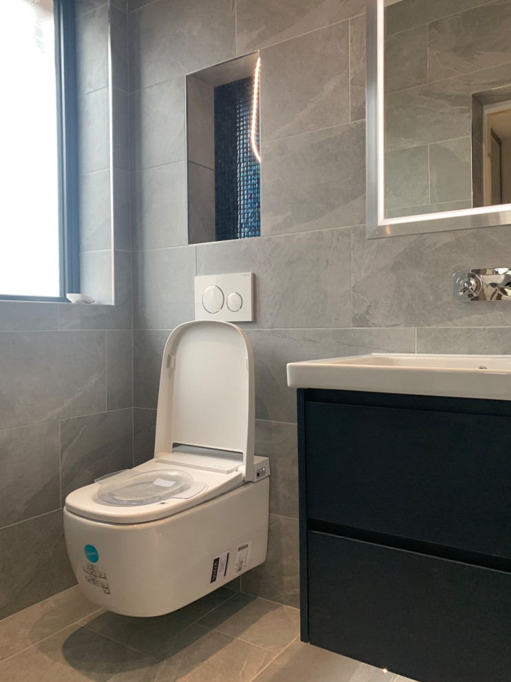 Example of a mid-sized master gray tile and porcelain tile porcelain tile, gray floor, double-sink and coffered ceiling bathroom design in Hertfordshire with flat-panel cabinets, blue cabinets, a wall-mount toilet, gray walls, a wall-mount sink, a niche and a floating vanity