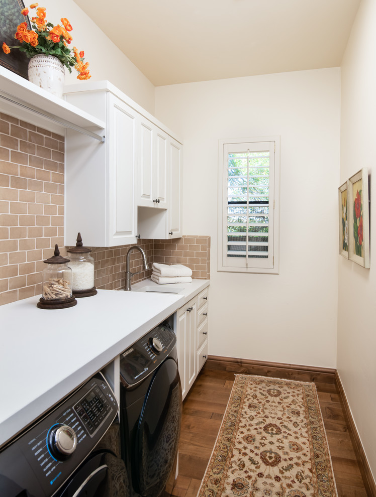 Mid-sized mediterranean galley dedicated laundry room in Phoenix with an undermount sink, raised-panel cabinets, white cabinets, concrete benchtops, white walls, medium hardwood floors, a side-by-side washer and dryer, brown floor and white benchtop.