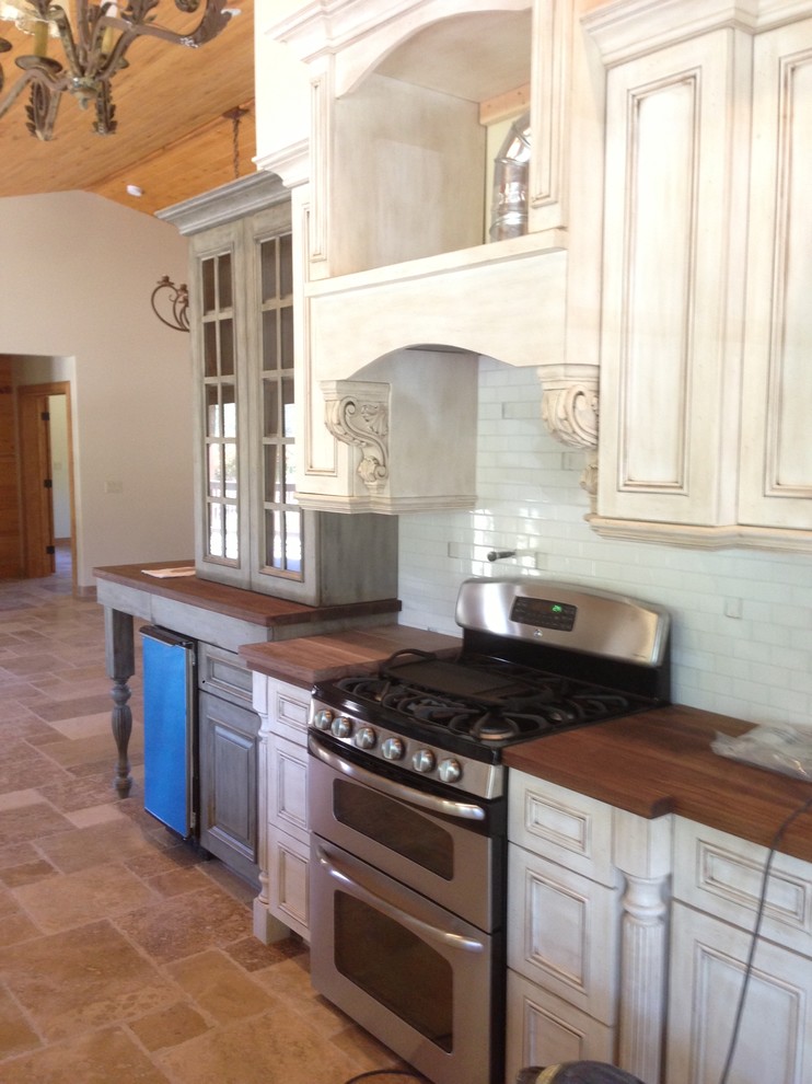 Open concept kitchen - mid-sized transitional limestone floor and beige floor open concept kitchen idea in Phoenix with recessed-panel cabinets, distressed cabinets, wood countertops, white backsplash, subway tile backsplash and stainless steel appliances