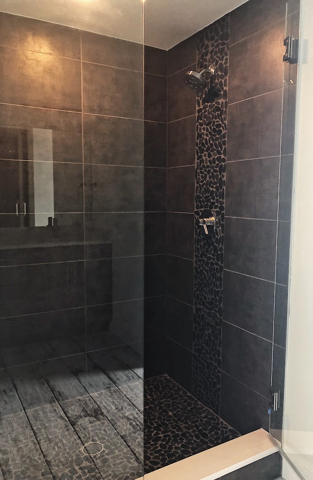 Industrial master bathroom in Denver with porcelain tile, brown walls, pebble tile floors, black floor and a hinged shower door.