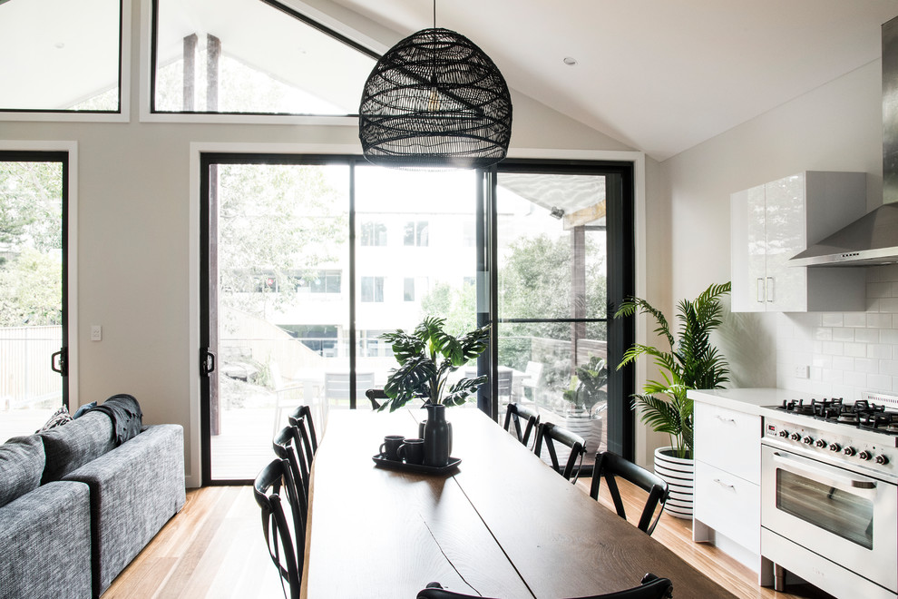This is an example of a mid-sized contemporary single-wall open plan kitchen in Sydney with solid surface benchtops, white splashback, subway tile splashback, stainless steel appliances, medium hardwood floors, no island and white benchtop.