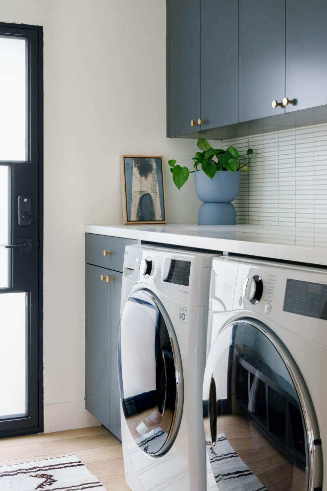 Large contemporary single-wall dedicated laundry room in San Diego with flat-panel cabinets, blue cabinets, quartz benchtops, white splashback, subway tile splashback, white walls, a side-by-side washer and dryer, white benchtop, light hardwood floors and beige floor.