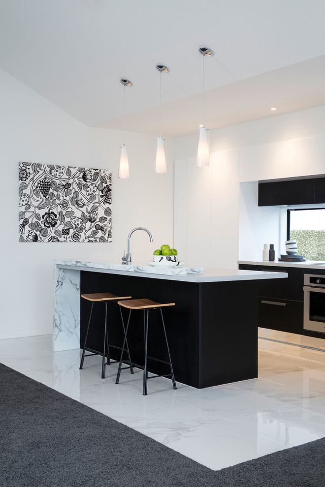 This is an example of a mid-sized modern galley open plan kitchen in Christchurch with flat-panel cabinets, black cabinets, marble benchtops, stainless steel appliances, porcelain floors, with island and white floor.