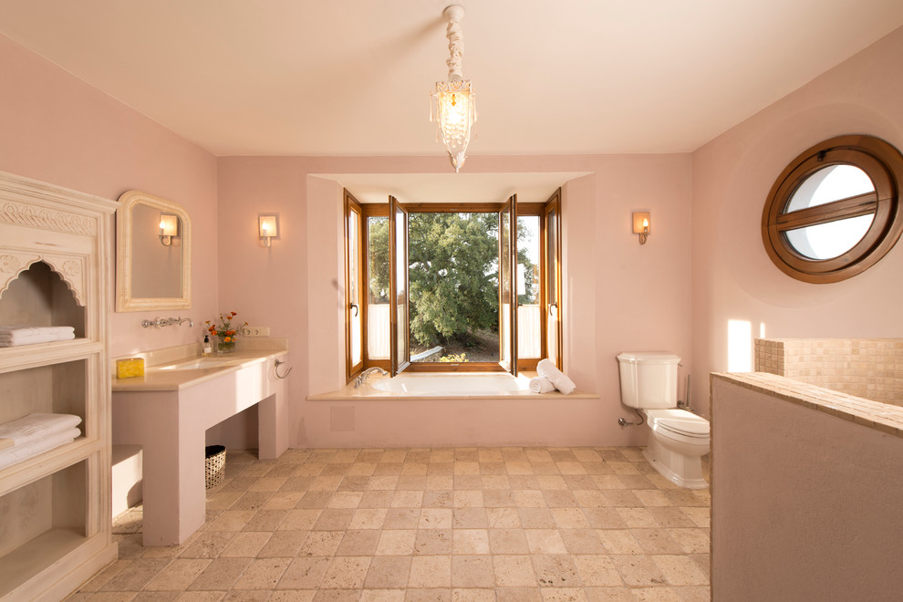 Inspiration for a mid-sized country 3/4 bathroom in Other with light wood cabinets, an open shower, beige tile, stone tile, pink walls, an undermount sink, a two-piece toilet, open cabinets, limestone floors and an open shower.