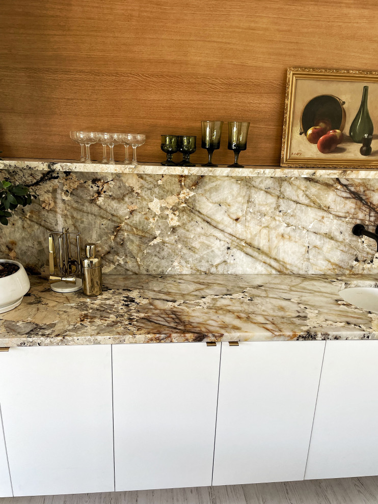 Design ideas for a small contemporary u-shaped home bar in Phoenix with an undermount sink, flat-panel cabinets, white cabinets, quartzite benchtops, beige splashback, granite splashback, light hardwood floors, white floor and beige benchtop.