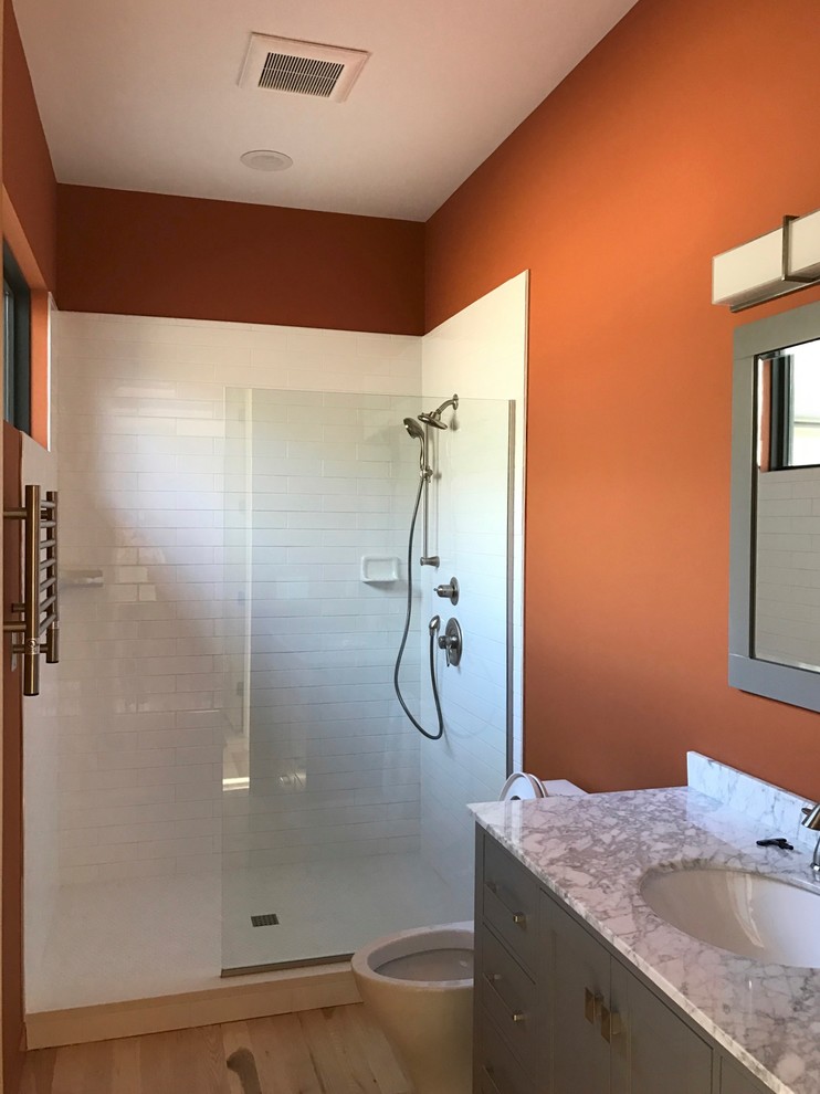 Inspiration for a small modern master bathroom in Raleigh with flat-panel cabinets, dark wood cabinets, an alcove shower, a one-piece toilet, white tile, ceramic tile, orange walls, light hardwood floors, an undermount sink and solid surface benchtops.
