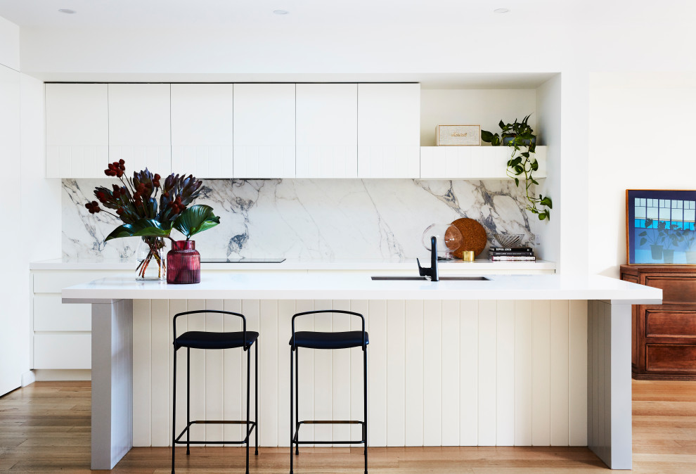 Contemporary galley kitchen in Melbourne with an undermount sink, flat-panel cabinets, white cabinets, white splashback, stone slab splashback, light hardwood floors, with island, beige floor and white benchtop.