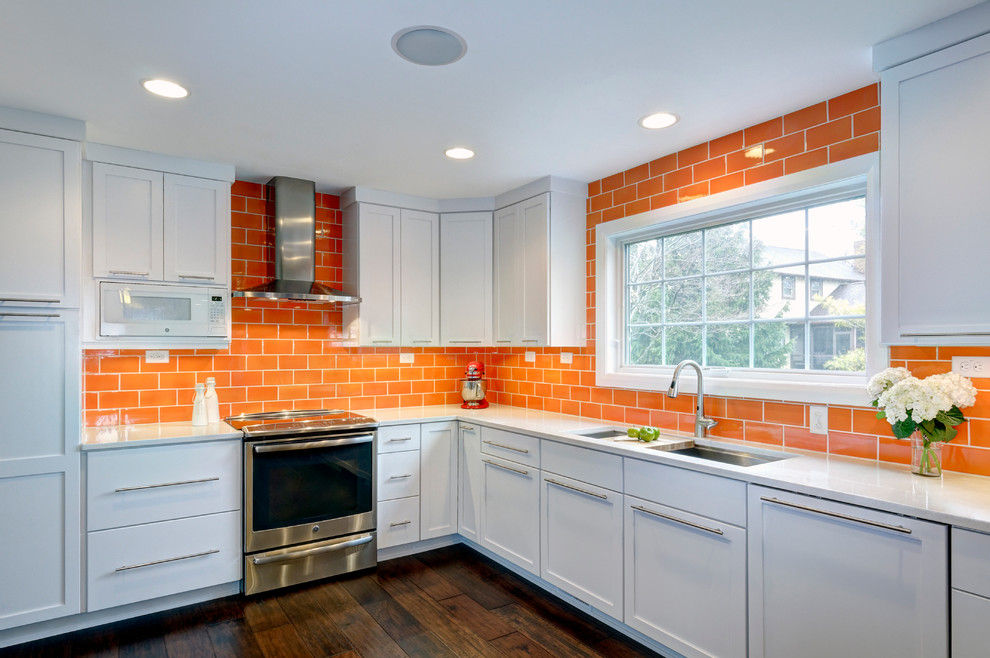 Photo of a contemporary l-shaped eat-in kitchen in Columbus with an undermount sink, flat-panel cabinets, white cabinets, quartz benchtops, orange splashback, ceramic splashback, stainless steel appliances, dark hardwood floors and a peninsula.