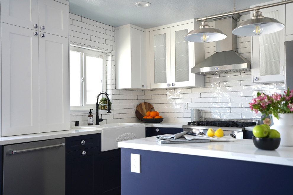 This is an example of a mid-sized beach style l-shaped eat-in kitchen in Orange County with a farmhouse sink, shaker cabinets, blue cabinets, quartz benchtops, white splashback, subway tile splashback, stainless steel appliances, ceramic floors, with island, multi-coloured floor, white benchtop and wallpaper.