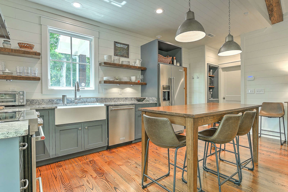 Photo of a small country l-shaped eat-in kitchen in Other with a farmhouse sink, flat-panel cabinets, grey cabinets, granite benchtops, shiplap splashback, stainless steel appliances, medium hardwood floors, no island, grey benchtop and timber.