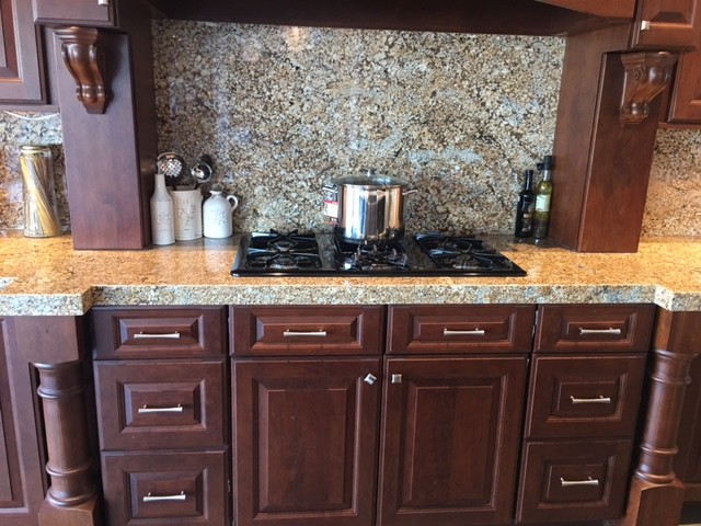 Example of a mid-sized trendy u-shaped kitchen design in Orange County with a farmhouse sink, raised-panel cabinets, medium tone wood cabinets, granite countertops, beige backsplash, stone tile backsplash and a peninsula