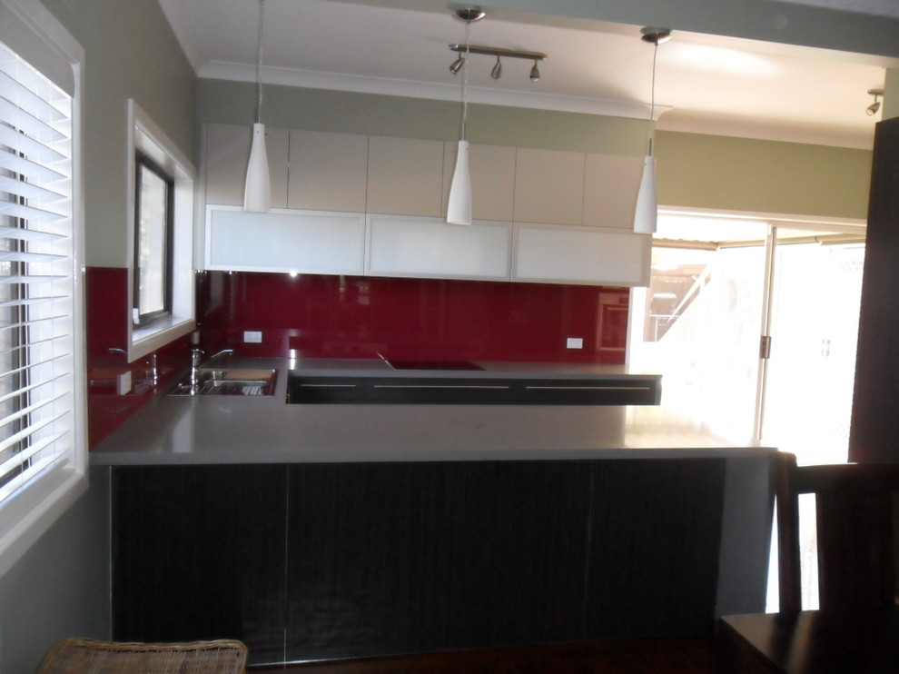 Inspiration for a mid-sized modern u-shaped eat-in kitchen in Sydney with a drop-in sink, quartz benchtops, red splashback, glass sheet splashback, stainless steel appliances, light hardwood floors and a peninsula.