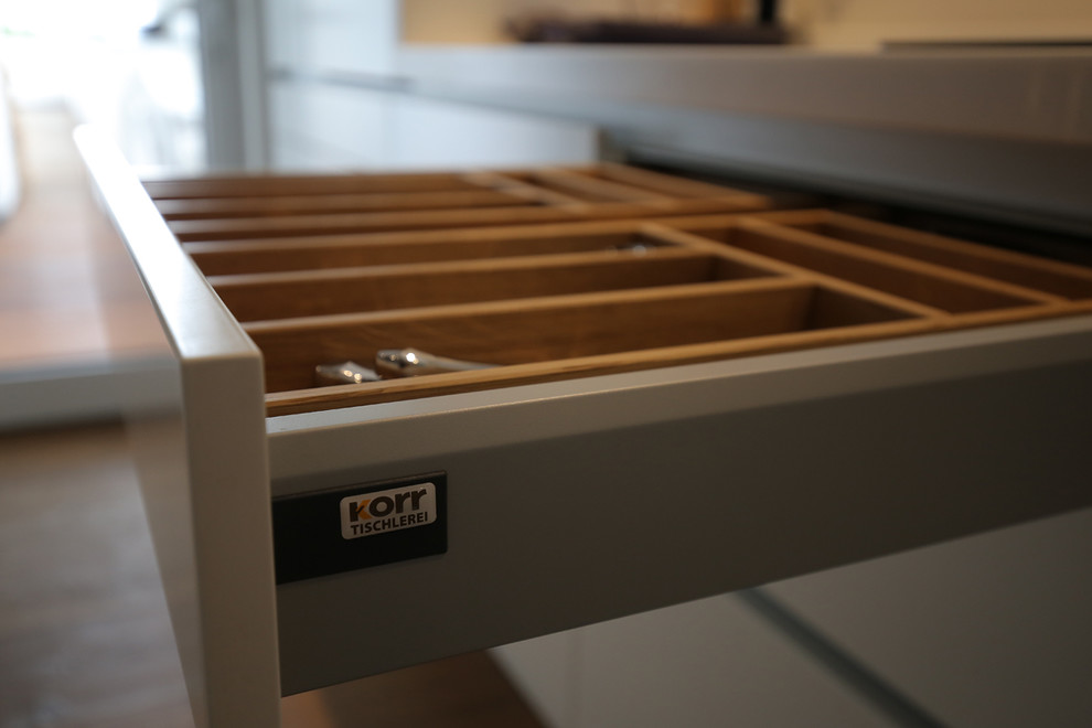 Moderne Küche mit weißen Schränken und braunem Holzboden in Köln