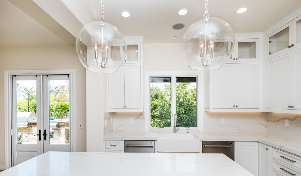Mid-sized transitional l-shaped porcelain tile and beige floor enclosed kitchen photo in Orange County with a farmhouse sink, recessed-panel cabinets, white cabinets, quartz countertops, white backsplash, marble backsplash, stainless steel appliances and an island