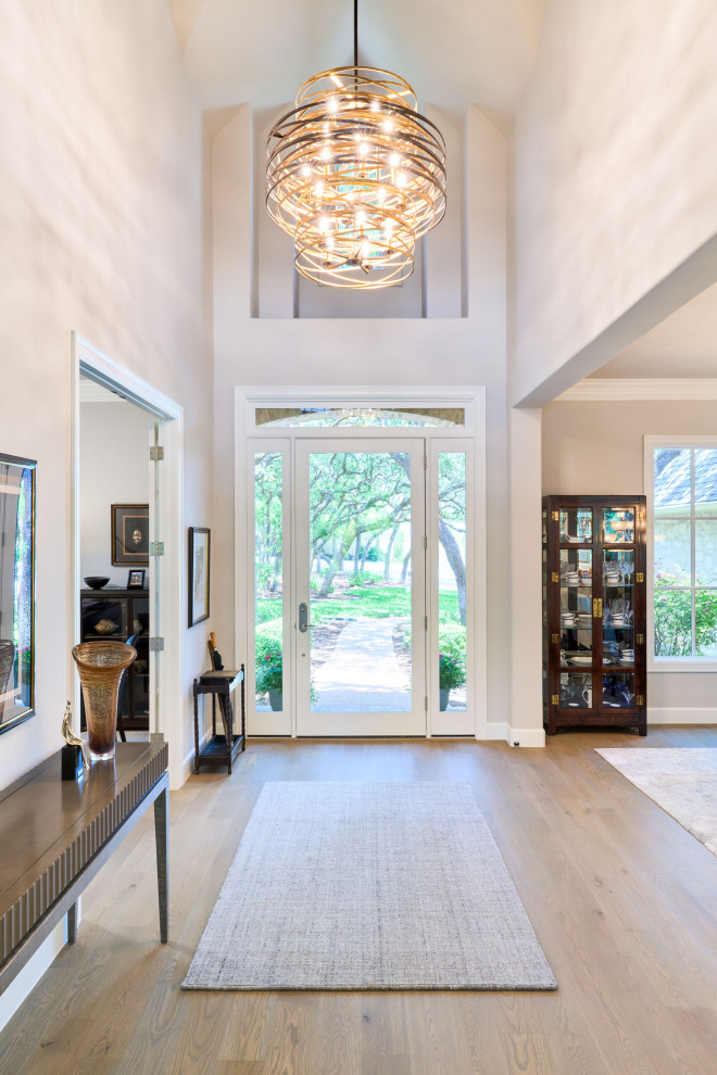 Design ideas for a medium sized traditional foyer in Austin with white walls, light hardwood flooring, a single front door, a glass front door, white floors and a vaulted ceiling.