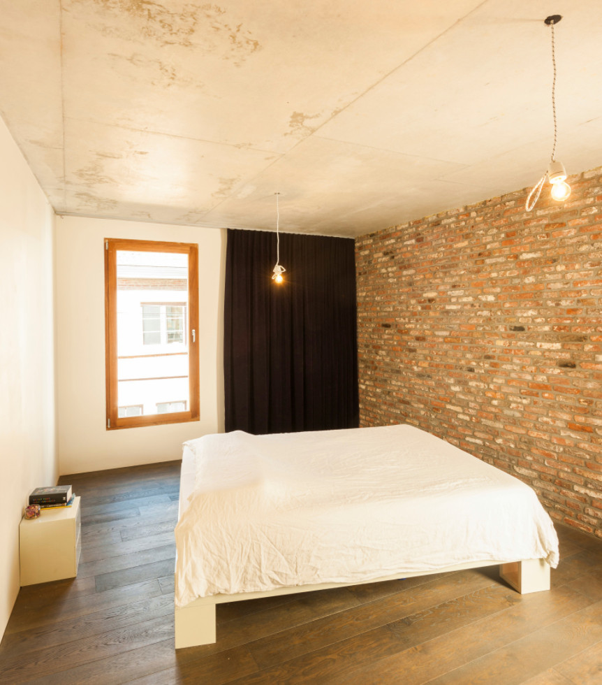 Inredning av ett amerikanskt stort sovrum, med vita väggar, mörkt trägolv, en spiselkrans i betong och brunt golv