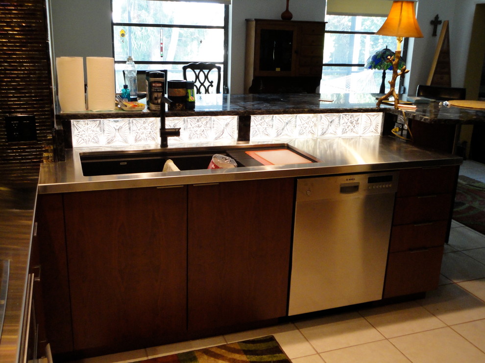 Photo of a contemporary kitchen in Tampa with an undermount sink, flat-panel cabinets, medium wood cabinets, stainless steel benchtops, black splashback, mosaic tile splashback, stainless steel appliances and ceramic floors.
