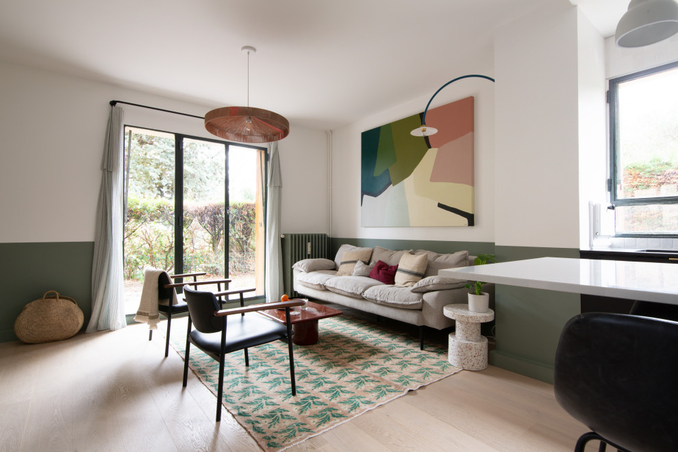 На фото: большая открытая гостиная комната в современном стиле с зелеными стенами, светлым паркетным полом, скрытым телевизором и коричневым полом без камина с