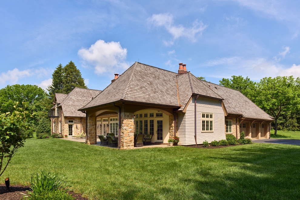 Aménagement d'une façade de maison beige classique en pierre à un étage avec un toit à croupette, un toit en shingle et un toit marron.