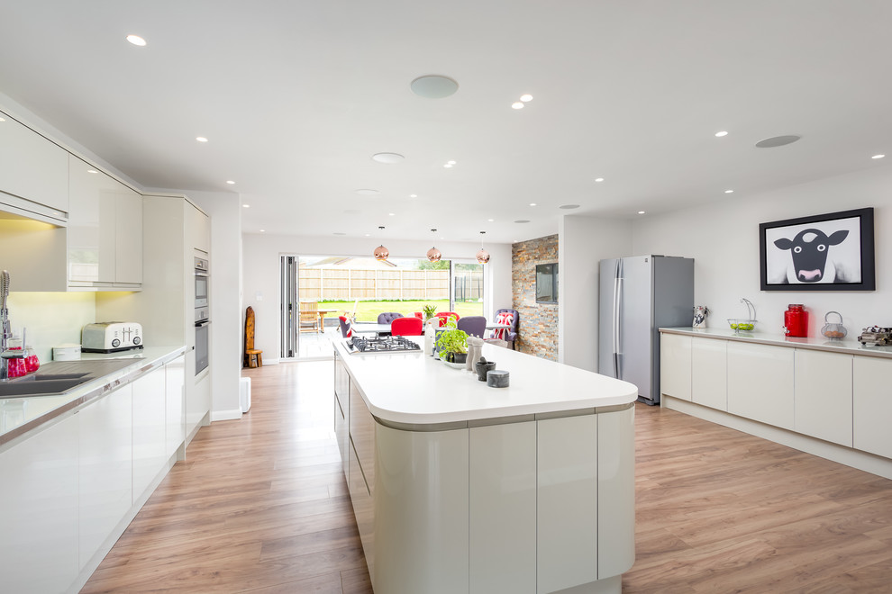 Inspiration for a large contemporary galley open plan kitchen in Gloucestershire with flat-panel cabinets, white cabinets, white appliances, a peninsula, brown floor, white benchtop and a drop-in sink.