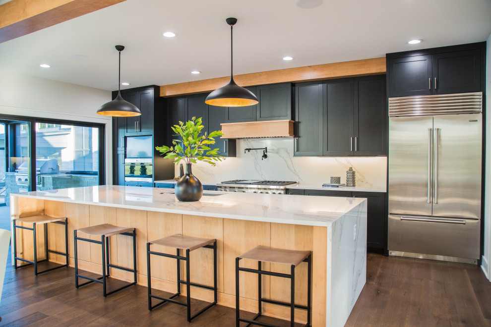 Expansive contemporary single-wall eat-in kitchen in Indianapolis with an undermount sink, recessed-panel cabinets, black cabinets, quartzite benchtops, white splashback, stone slab splashback, stainless steel appliances, medium hardwood floors, with island, brown floor, white benchtop and exposed beam.