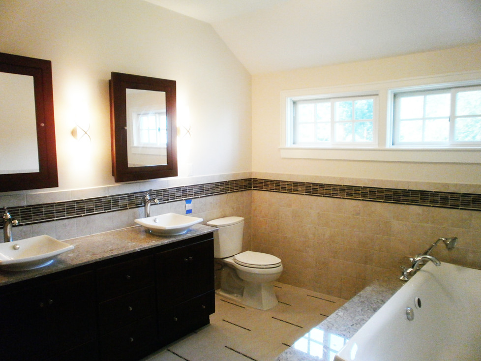 Large traditional master bathroom in Providence with a vessel sink, flat-panel cabinets, dark wood cabinets, granite benchtops, a drop-in tub, a one-piece toilet, beige tile, stone tile, beige walls and travertine floors.