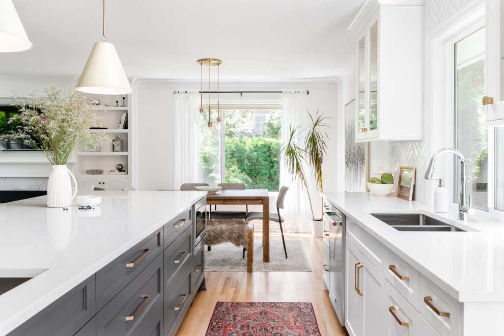 Open concept kitchen - large transitional l-shaped light wood floor and beige floor open concept kitchen idea in Vancouver with an undermount sink, recessed-panel cabinets, white cabinets, quartz countertops, white backsplash, ceramic backsplash, stainless steel appliances, an island and white countertops