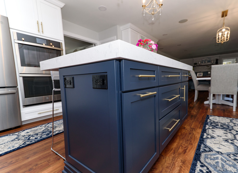 Example of a mid-sized transitional galley brown floor and medium tone wood floor eat-in kitchen design in Baltimore with shaker cabinets, white cabinets, quartz countertops, white backsplash, subway tile backsplash, stainless steel appliances, an island, white countertops and an undermount sink