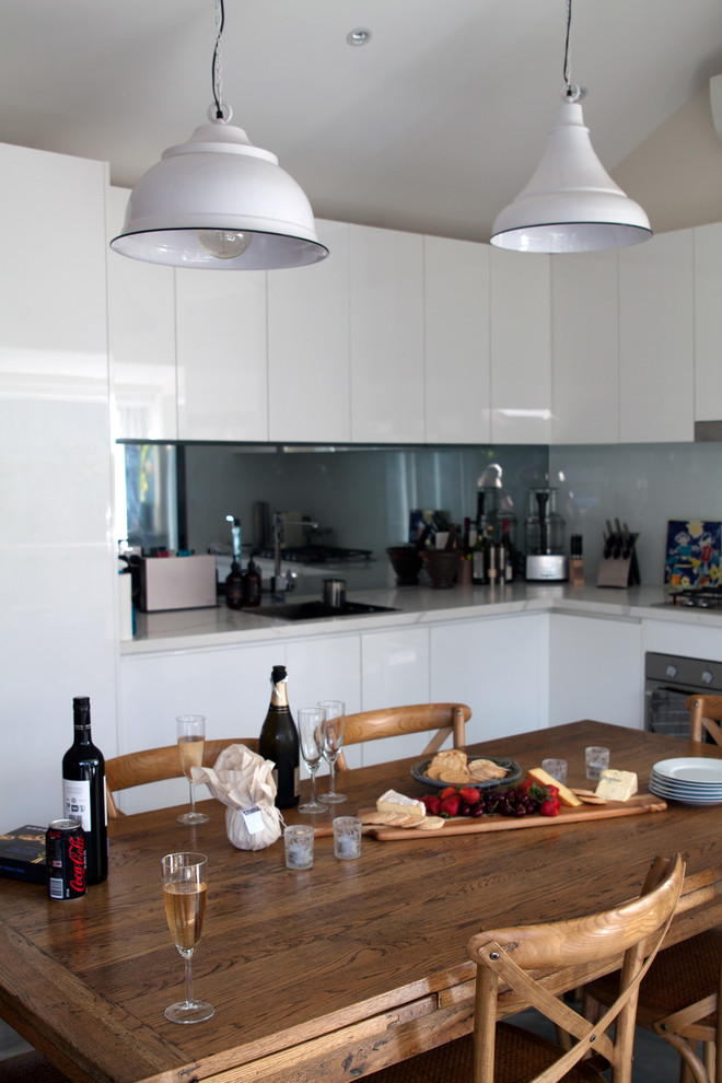 This is an example of a tropical l-shaped open plan kitchen in Other with an undermount sink, white cabinets, quartz benchtops, white splashback, glass sheet splashback, stainless steel appliances, concrete floors and with island.